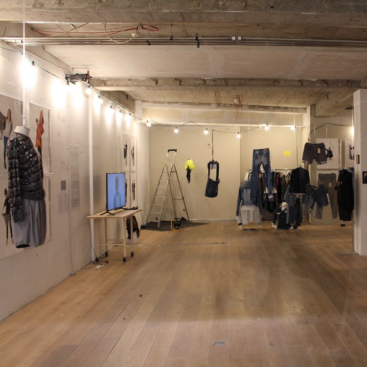 Das Bild zeigt einen Raum des Instituts. In diesem wurde eine Auststellung aufgebaut. Verschiedene Jeans-Kleidungsstücke hängen von der Decke und Plakate kleben an der Wand