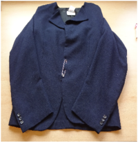 Objektfoto. Auf dem Tisch liegender Blazer. In der Mitte ist dieser mit einer großen Sicherheitsnadel geschlossen