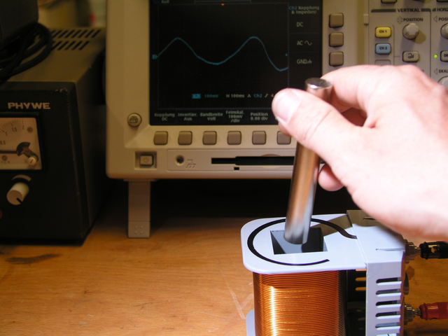 Ein starker Dauermagnet wird in einer Spule bewegt und die induzierte Spannung auf dem Oszilloskop gemessen. Foto eines Dauermagneten der in einer Spule bewegt wird.