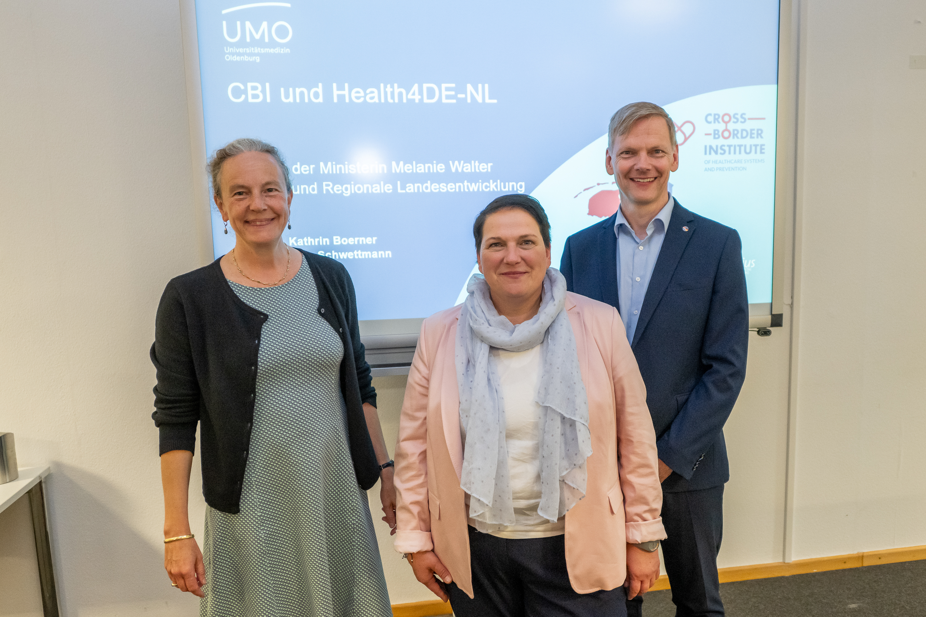 Prof. Dr. Kathrin Boerner, Minister Melanie Walter and Prof. Dr. Lars Schwettmann in front of the presentation