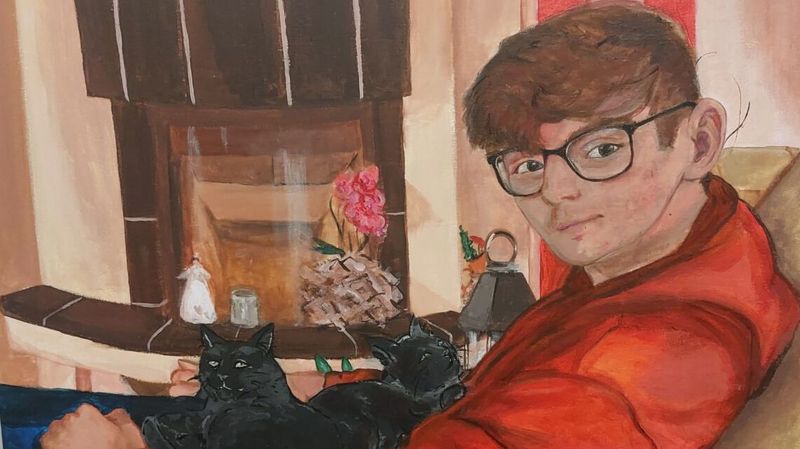 Das Gemälde eines jungen Mannes der vor dem Betrachter auf dem Sofa sitzt und sich zum Betrachter umdreht. Der Mann trägt ein rotes Shirt und Brille, auf seinem Schoß eine schwarze Katze, im Hintergrund ein Kamin, in dem kein Feuer brennt.