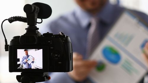 Mann mit Präsentationsblatt durch eine Kamera 