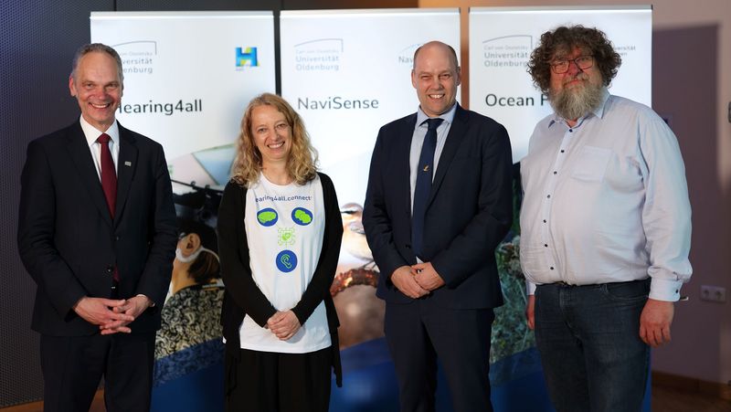 Vier Personen stehen nebeneinander vor drei Roll-ups der einzelnen Cluster. 