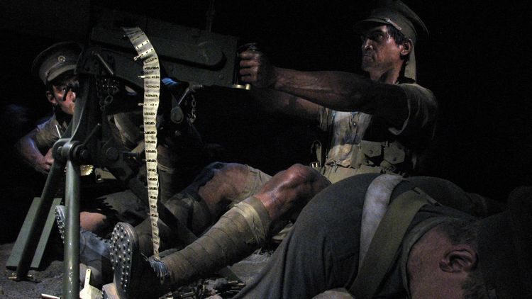 The picture shows a wax figure of a soldier firing a machine gun. The figure is surrounded by other soldiers, at least one of whom appears to be dead. The machine-gunner looks grim.