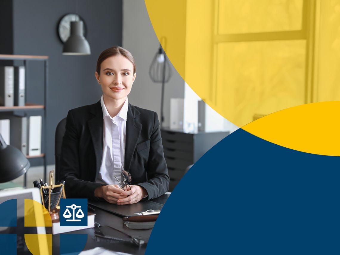 Eine Frau im Anzug sitzt in einem Büro und lächelt in die Kamera.