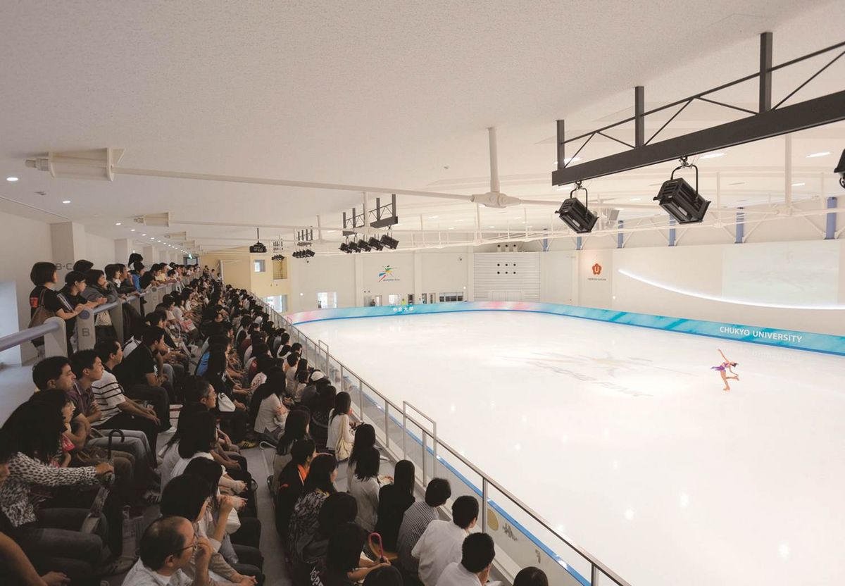 Eine Eislaufbahn mit Zuschauer*innen auf den Rängen. Eine Person läuft auf dem Eis, während andere zusehen. Die Eislaufbahn, die sich auf dem Toyota Campus befindet, ist von blauen und weißen Barrieren umgeben.