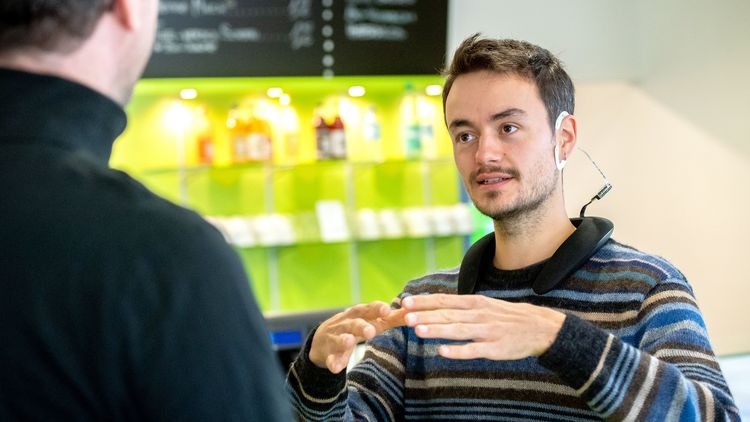 Zwei Personen im alltäglichen Gespräch, bei dem eine Person ein cEEGrid und das damit verbundene Equipment trägt.