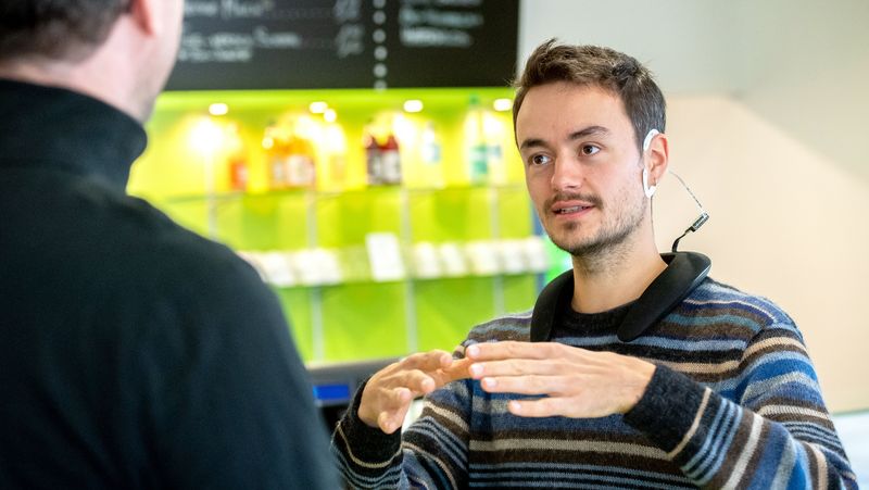 Zwei Personen im alltäglichen Gespräch, bei dem eine Person ein cEEGrid und das damit verbundene Equipment trägt.