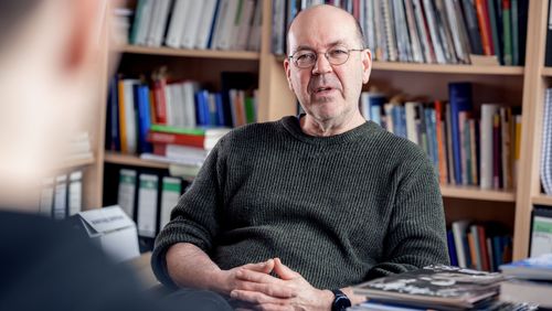 The picture shows Dietmar von Reeken. He is sitting in front of a bookshelf and talking to the interviewer.