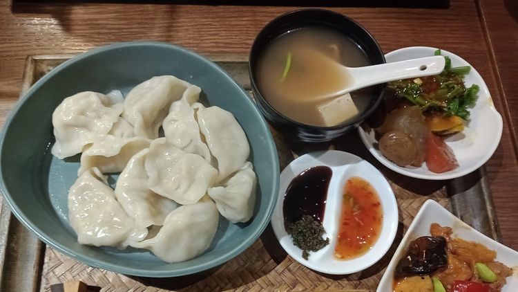 Ein Tablett mit mehreren Tellern und Schälchen, gefüllt mit Teigtaschen, einer Suppe, Saucen und anderen Beilagen.