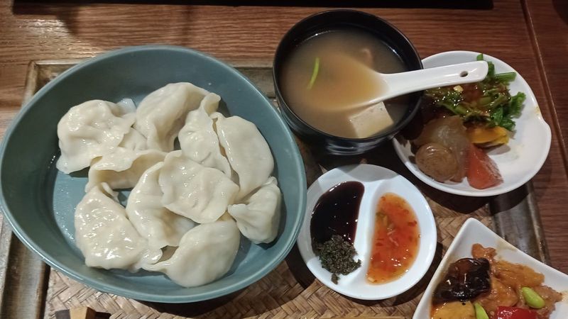 Ein Tablett mit mehreren Tellern und Schälchen, gefüllt mit Teigtaschen, einer Suppe, Saucen und anderen Beilagen.