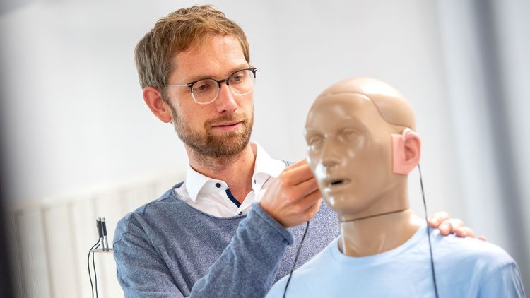 Kai Siedenburg im Hörlabor mit einer schaufensterartigen Puppe, die Hörgeräte trägt.