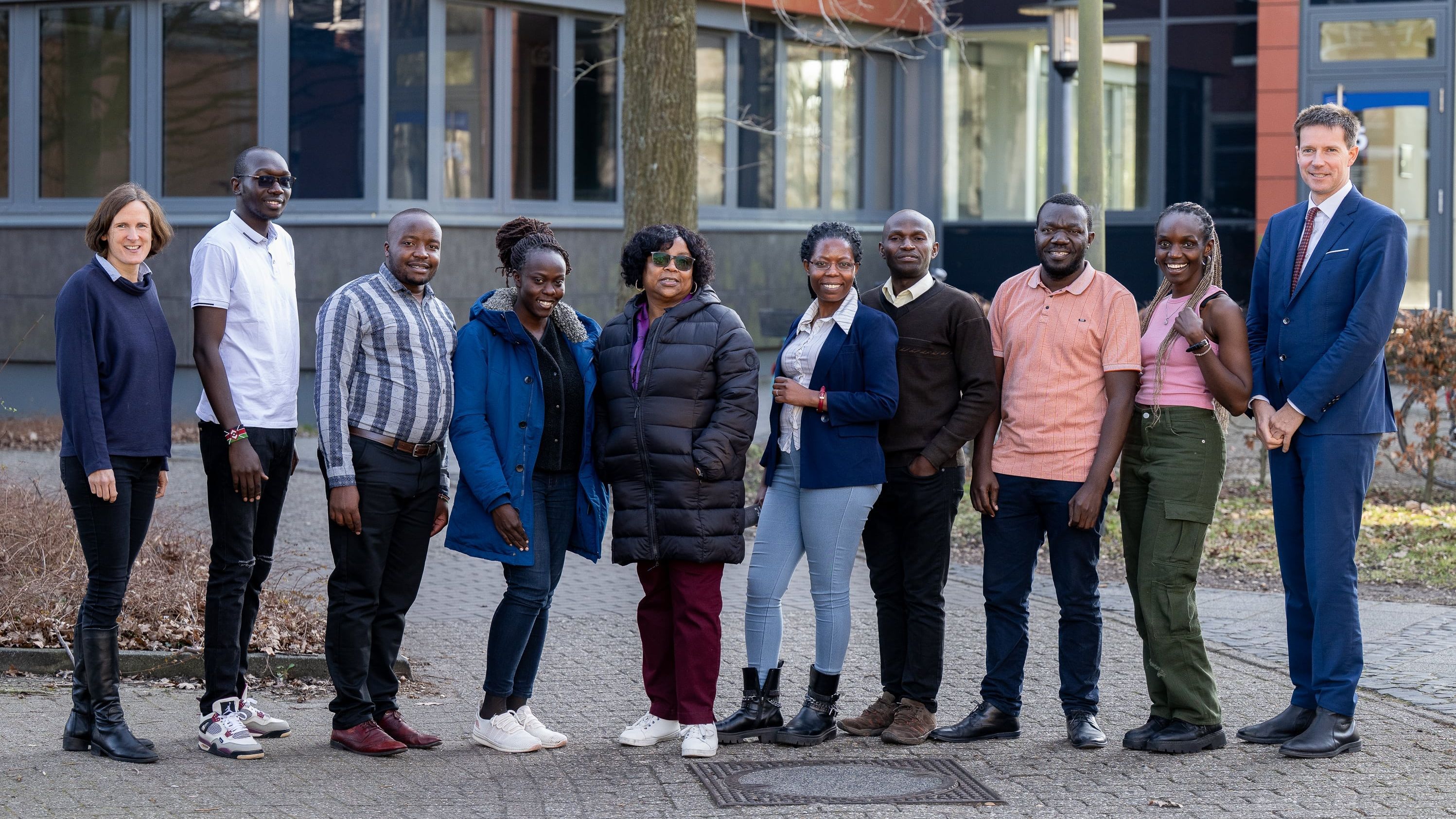 The picture shows a group of DAAD scholarship holders. Malve von Möllendorff and Karsten Speck are standing with them in front of a university building, all smiling at the camera. There are ten people in total.