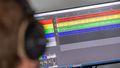 A person sits with headphones in front of a screen on which various sound tracks can be seen.