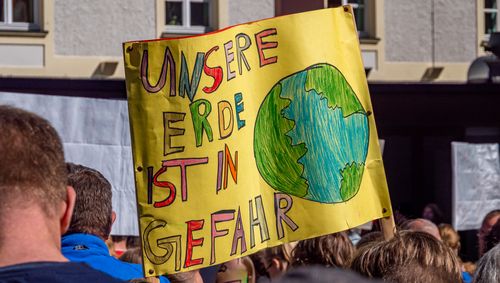 Das Bild stammt von einer Demo der Bewegung Fridays for Future. Im Zentrum ist ein großes, selbstgemaltes Plakat mit einer Erdkugel zu sehen, auf dem steht: Unsere Erde ist in Gefahr. 