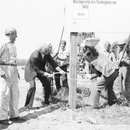 Das Bild zeigt den damaligen Minister für Wissenschaft und Kunst Eduard Pestel und den kommissarischen Unipräsidenten Hans-Dietrich Raapke, wie sie die Proteststellwand als symbolträchtigen Akt gemeinsam absägen. Umstehende schauen sich die Arbeit an.