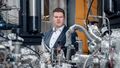 A young man stands behind a complicated system consisting of numerous tubes, valves and hoses wrapped in aluminium foil.