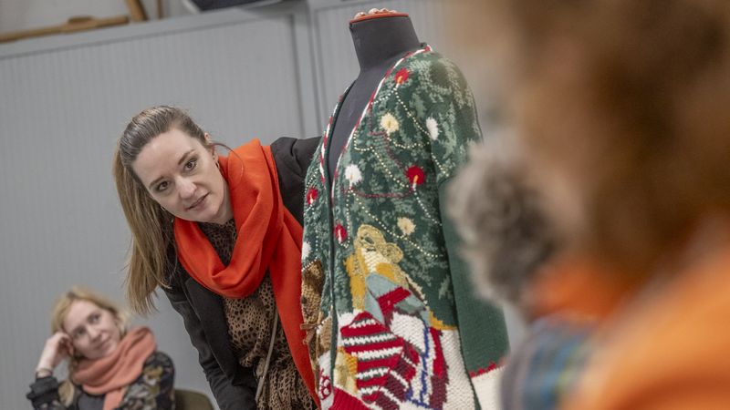 Eine wild gemusterte Strickjacke hängt über einer Art Schaufensterpuppe, dahinter schaut Klara von Lindern hervor. 
