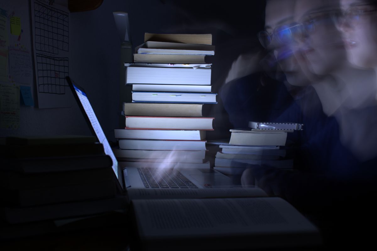 Forschen für Nachteulen — Irma Reich — Die blaue Färbung greift unter anderem die Farbe unserer Uni auf und der Laptop als einzige Lichtquelle spiegelt die Digitalisierung wider. Durch die mehrmals übereinander abgebildete Person (Langzeitbelichtung, keine Fotobearbeitung) wird repräsentiert, wie dynamisch der Denkprozess beim Forschen ist, während durch die Statik der Bücher die Vielschichtigkeit und Konstanz, die beim Forschen notwendig ist, zum Ausdruck kommt. Es handelt sich dabei um ein Selbstportrait, das heißt, alles Abgebildete ist tatsächlich Teil meiner Masterarbeit und bildet authentisch einen Großteil meines Forschungsprozesses ab. 
