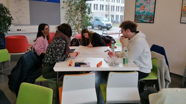 Das Bild zeigt eine Gruppe von Studierenden bei einem Workshop im Interkulturellen Treff der Uni. Sie arbeiten an einem Poster.