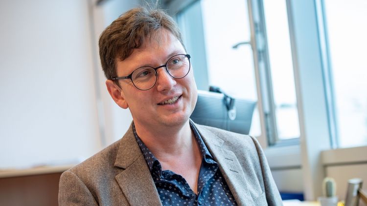 Mark Schweda im Gespräch. er trägt eine Brille, ein hellbraunes Sakko und ein blaues, gemustertes Hemd.