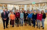 The photo shows the group of the network. A total of 15 people can be seen lined up in two rows in a slight arc. The picture was taken in the foyer of the library, the entrance area of which can be seen in the background.