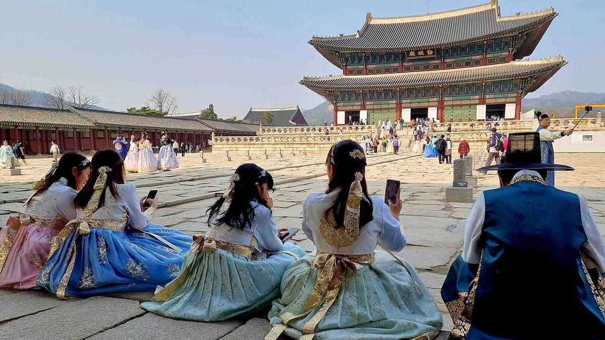 Menschen am Gyeongbokgung Palast in Seoul Eine Gruppe von Menschen in Hanboks vor dem Gyeongbokgung Palast in Seoul. Frauen sitzen auf dem Hof und machen Fotos