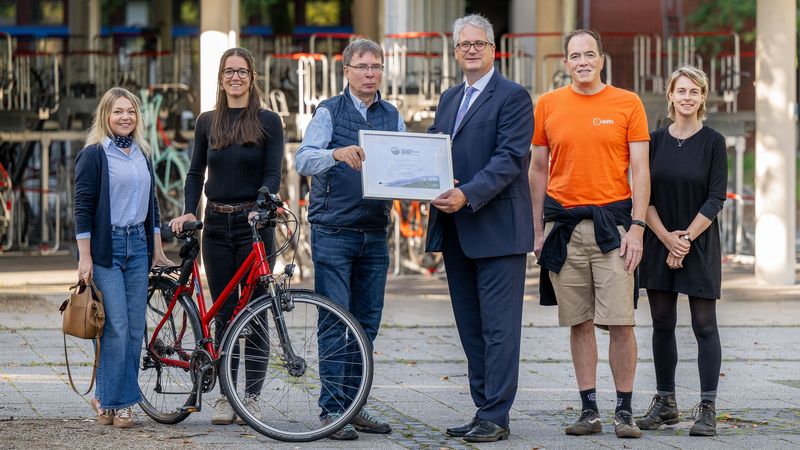 Sechs Menschen stehen nebeneinander mit einem Fahrrad und einem Zertifikat.