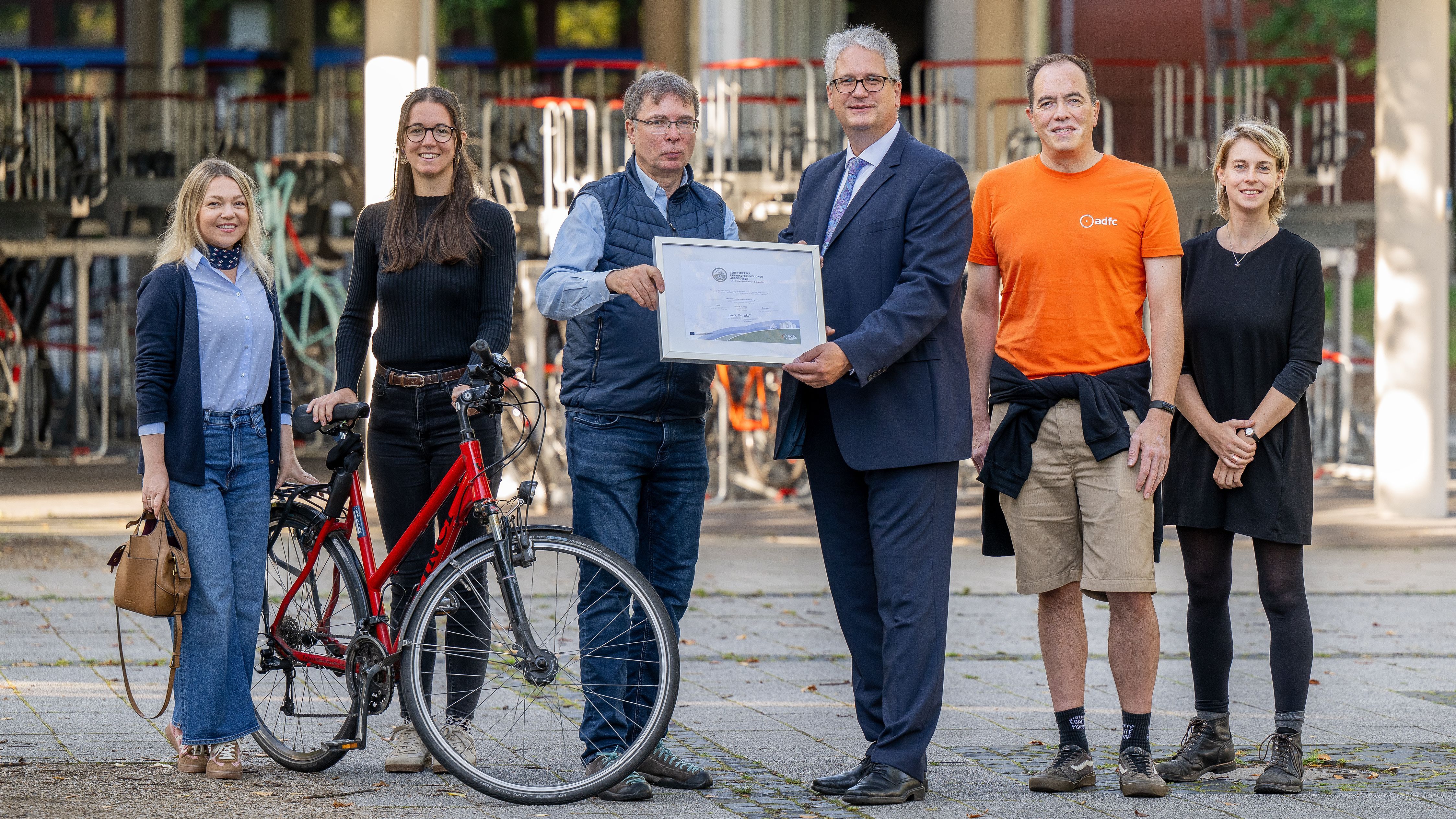 Six people stand next to each other with a bicycle and a certificate..