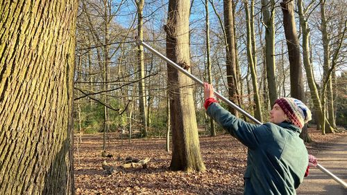 Ein junger Mann hält eine lange Stange in der Hand. Vorne befindet sich ein Plättchen, das am Baum befestigt werden soll.  