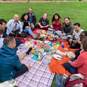 Trip to Bad Zwischenahn A group of 10 people having a picnic on a checkered blanket in a park.
