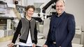 The picture shows Miriam Liedvogel and Henrik Mouritsen. They stand in front of technical equipment in a laboratory and smile into the camera.