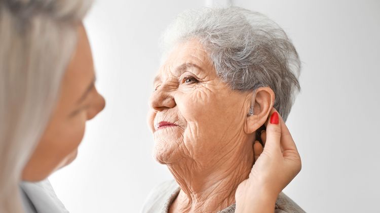 Junge Frau passt älterer Frau ein Hörgerät an.