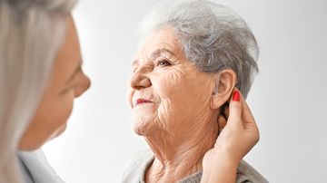 A young woman fits an older woman with a hearing aid.
