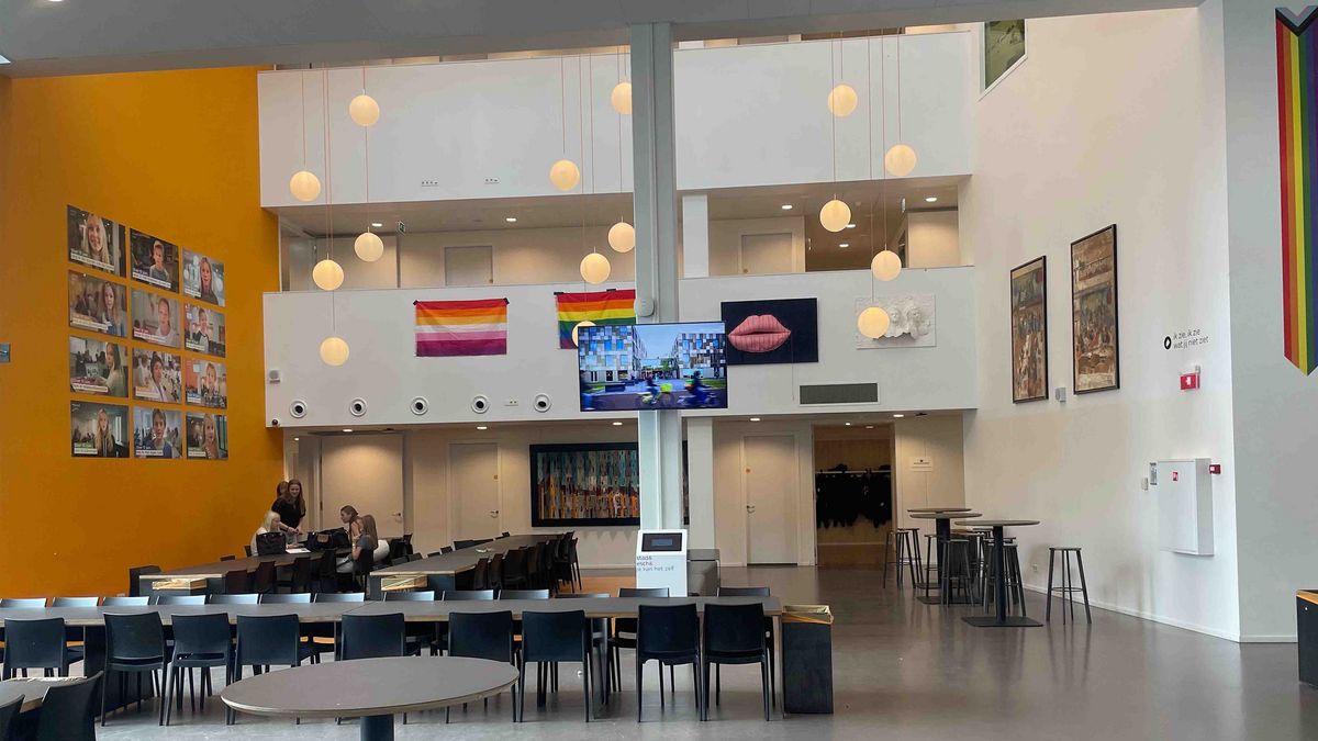 Teaching Across Borders A large, light corridor in the Schule Stad&Esch with portraits, artworks and rainbow flags. A large screen with video in the center.