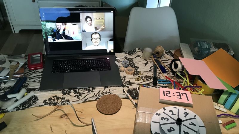 Ein Schreibtisch mit aufgeklapptem Laptop, daneben Materialien wie Schnüre, Schwämme, Kleber, Schere, Stoff.