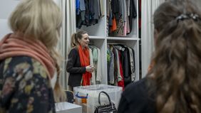 Die Kustodin steht vor den raumhohen Schränken, in denen alle Arten von Kleidungsstücken hängen.