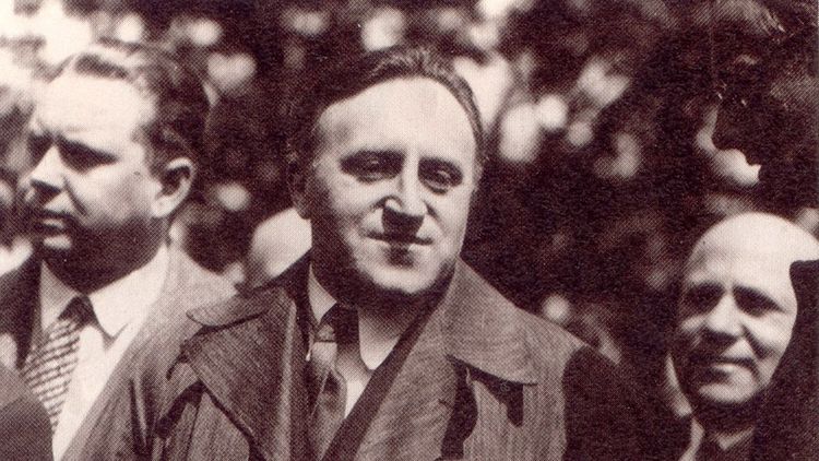 Das Bild zeigt Carl von Ossietzky neben anderen Männern. Er trägt einen Anzug, Krawatte und Mantel.