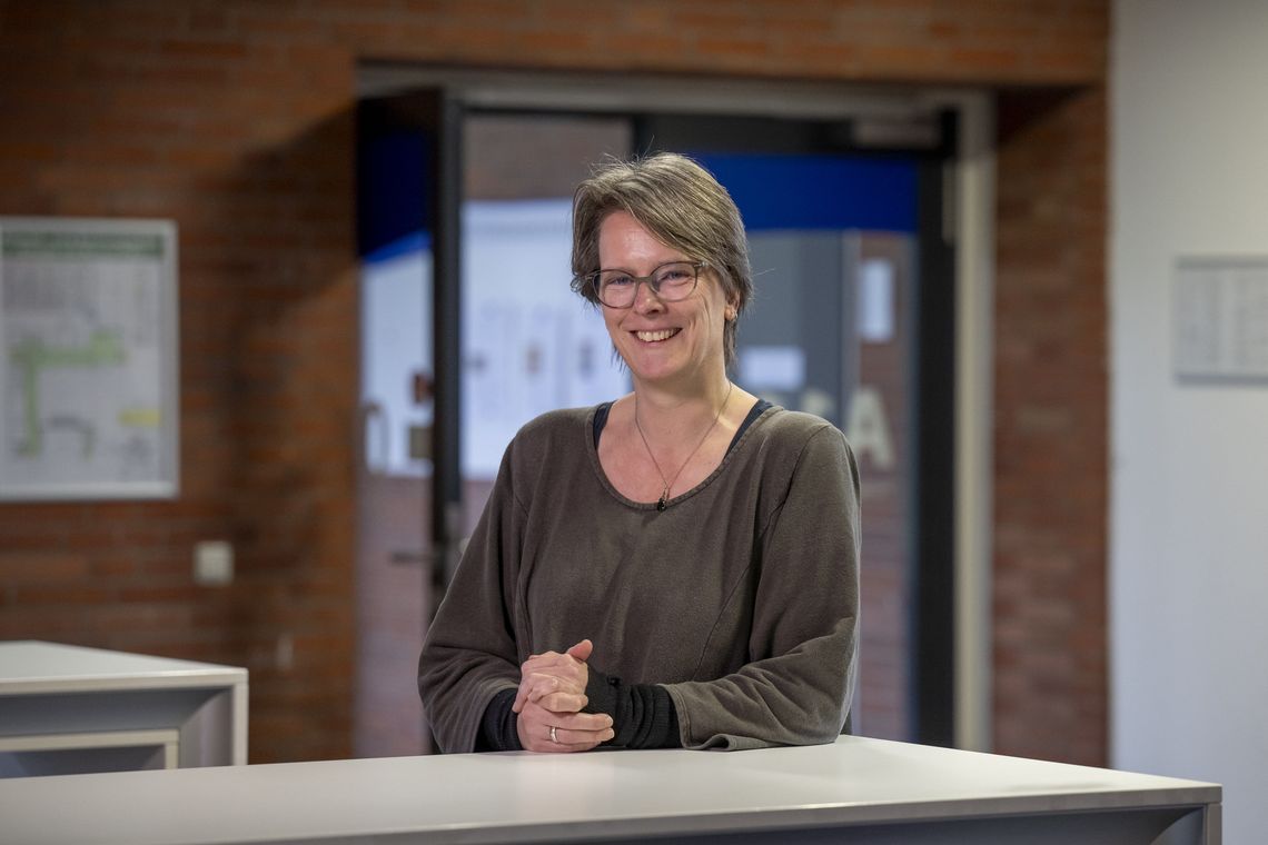 Das Bild zeigt Esther Ruigendijk. Sie stützt ihre Arme auf einem Tisch ab und lächelt in die Kamera.
