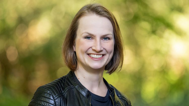 Das Bild zeigt Frau Pöppel. Sie lächelt in die Kamera. Im Hintergrund sind Bäume zu erkennen.