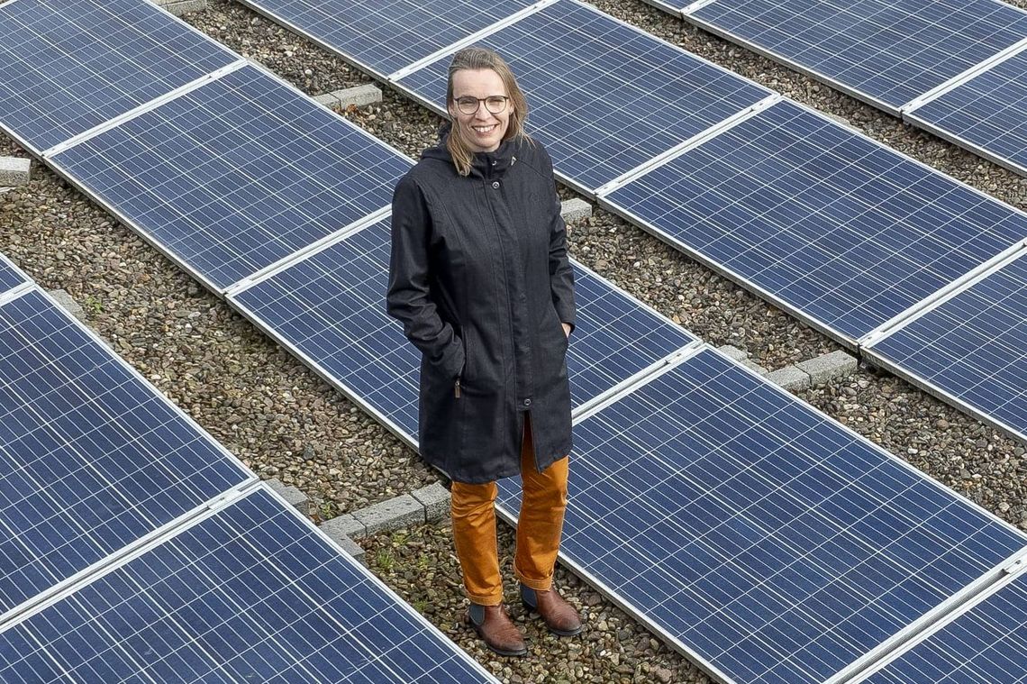 Astrid Nieße steht auf dem Dach der Verbindungsbrücke zwischen dem Mensatrakt und A1-4. Sie ist umgeben von Photovoltaikanlagen, die sich das komplette Dach entlang erstrecken. Nieße lächelt in die Kamera.