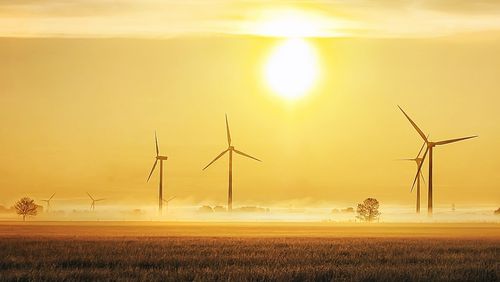 Mehrere Windräder im Gegenlicht bei Sonnenuntergang. 