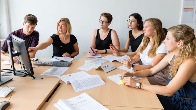 Eine Gruppe von fünf Wissenschaftlerinnen und einem Wissenschaftler sitzt um einen Tisch und diskutiert über Forschungsergebnisse.