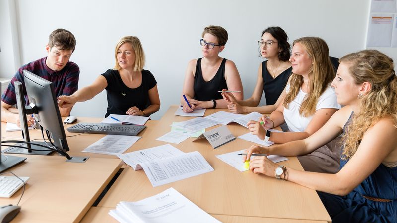 Eine Gruppe von fünf Wissenschaftlerinnen und einem Wissenschaftler sitzt um einen Tisch und diskutiert über Forschungsergebnisse.
