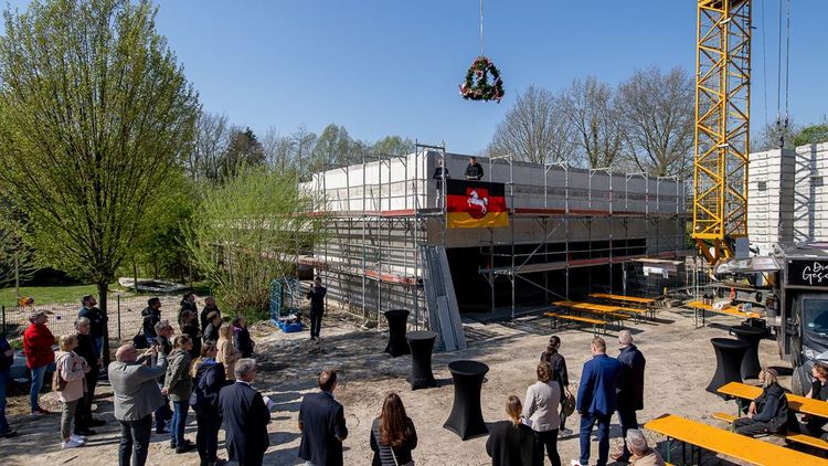 Totale auf den Rohbau, über dem der Richtkranz hängt. Einige Leute stehen um das Gebäude herum.
