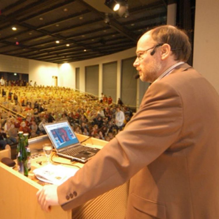 Das Bild zeigt Prof. Dr. Dr. Birger Kollmeier im Audimax bei seiner Vorlesung. Im Auditorium sitzen hunderte wissbegierige Kinder und lauschen seinen Ausführungen.