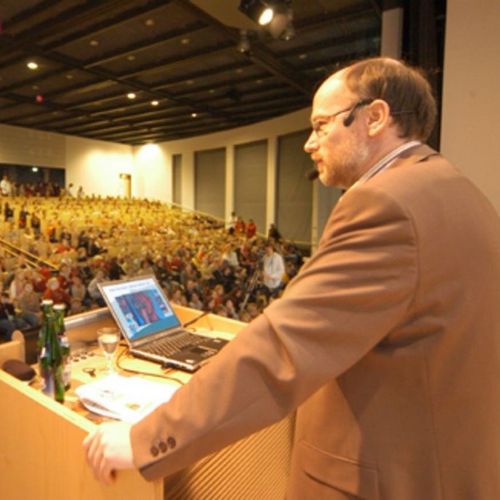 Das Bild zeigt Prof. Dr. Dr. Birger Kollmeier im Audimax bei seiner Vorlesung. Im Auditorium sitzen hunderte wissbegierige Kinder und lauschen seinen Ausführungen.