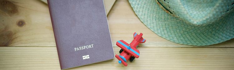 Symbolbild Visum Reisepass, Spielzeugflugzeug und Strohhut liegen auf einem Holztisch.