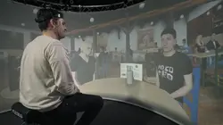 Ein Mann schaut auf eine Leinwand, auf der ein anderer Mann projiziert ist. 