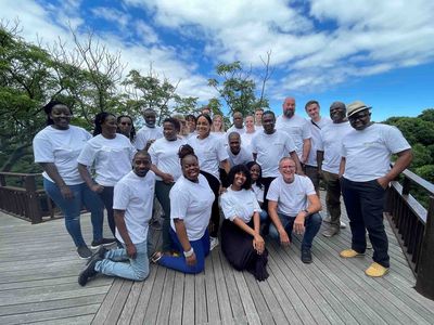 Projekttreffen der Oldenburger Informatik in Südafrika Eine Gruppe von Menschen steht auf einer Holzterrasse vor Bäumen. Sie tragen T-Shirts mit Aufdruck und scheinen an einem Projekttreffen teilzunehmen.